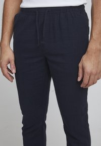 Navy drawstring broek gemaakt van textured stof met een elastische tailleband, voorzien van zijzakken en een tapered leg ontwerp.