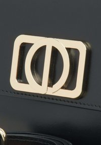 Černá kožená kabelka s kulatým detailem na zlatém obdélníkovém zapínání, hladkým povrchem a viditelným švem.