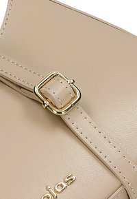 Sangle de sac en cuir beige avec une boucle carrée dorée, des coutures contrastées et un détail de logo métallique près du bas.