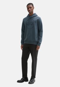 Felpa con cappuccio di colore blu scuro con stampa del logo, realizzata in tessuto morbido, abbinata a pantaloni neri e scarpe nere, con un design semplice.