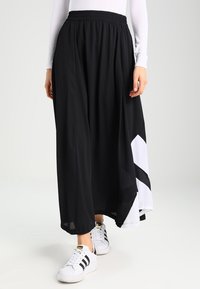 Svart, flödande maxi kjol med elastiskt midjeband. Har en diagonal vit detalj. Bärs med vita sneakers för en avslappnad look.