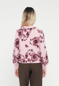 Blomstrete genser i myk rosa med mørkerøde og mauve aksenter, med rund hals og ribbestrikkede mansjetter.