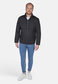 Sort puffjakke med quiltet struktur, lynlås, og opretstående krave, parret med lyseblå jeans og hvide sneakers.