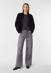 Schwarze Bomberjacke mit Reißverschluss über einem grauen T-Shirt, kombiniert mit hoch taillierten, weiten grauen Jeans und schwarzen Ankle Boots. Minimalistisches Design.