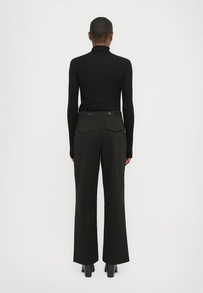 Un haut à col roulé noir associé à un pantalon noir taille haute. Caractéristiques : une texture lisse, une coupe droite et deux poches arrière.