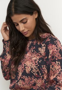 Maglia a maniche lunghe in blu navy con motivo floreale in tonalità di rosa e pesca. Presenta una scollatura rotonda e polsini arricciati. Tessuto dalla texture morbida.