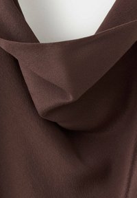 Gros plan d'un tissu tricoté brun foncé avec des plis souples et une texture légèrement surélevée.