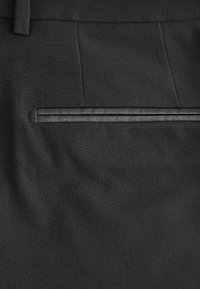 Pantalons noirs ajustés avec une texture lisse, dotés d'une poche latérale avec un élégant contour noir pour le détail et une coupe ajustée.
