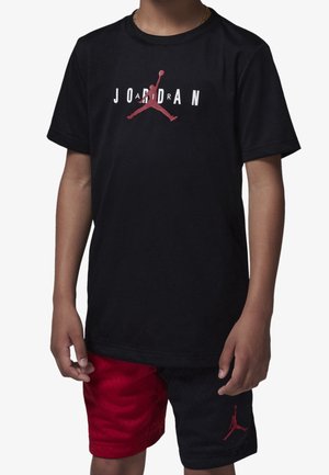 Dziecko w czarnej koszulce Jordan z czerwonym logo Jumpman oraz czarno-czerwonych spodenkach do koszykówki z czerwonym logo Jumpman.