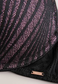 Material din dantelă negru cu model geometric suprapus peste un material roz, cu o etichetă metalică mică inscripționată „Lipsy” la marginea inferioară.