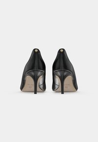 Scarpe alte in pelle nera con punta affusolata, caratterizzate da una finitura liscia e un tacco a stiletto stretto. Accento dorato sul retro.