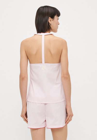 Haut sans manches rose clair avec un design à col halter, comportant une petite étiquette à l'arrière. Associé à un short assorti avec un liseré rouge.