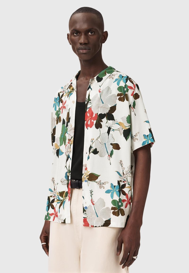 Chemise à manches courtes boutonnée blanche avec un imprimé floral vibrant en rouge, bleu, vert et marron. Présente une coupe décontractée et un col ouvert.