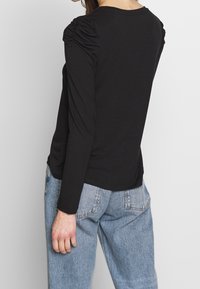 Haut noir à manches longues avec des détails froncés aux épaules, encolure ronde et coupe décontractée. Associé à un jean taille haute bleu clair.