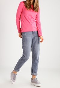 Maglietta a maniche lunghe rosa, vestibilità comoda, abbinata a jeans di denim blu chiaro, risvoltati alle caviglie, e sneakers grigie con suole bianche spesse.