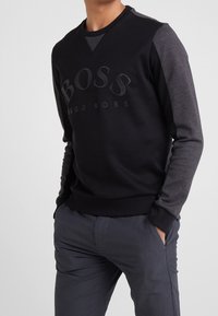 Crewneck-tröja i svart med mörkgrå ärmar. Har präglad "BOSS"-logotyp på framsidan. Slät tyg med ribbade muddar och fåll.