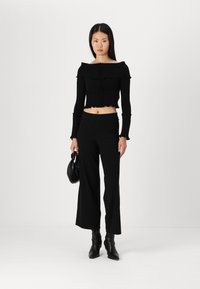 Crni rebrasti crop top bez ramena s volanima, uklopljen s crnim širokim hlačama i crnim čizmama s petom, držan malom torbicom.