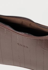 Bolsa con cremallera de textura marrón con líneas verticales sutiles, con forro interior marrón y un pequeño logo en relieve en el lateral.