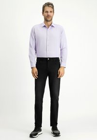 Camicia button-up viola chiaro con un motivo texturizzato, abbinata a jeans neri slim-fit e sneakers scure.