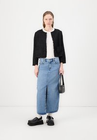 Svart tweedjakke med frynser, hvit topp, blå denim maxi-skirt med frontslit, og svarte platå-sko. Liten svart håndveske.