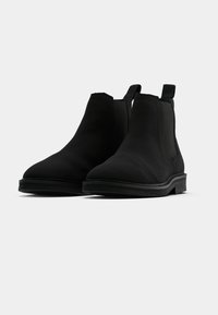 Černé chelsea boty z hladkého materiálu s elastickými bočními panely, poutkem na přetahování a texturovanou gumovou podrážkou. Zaoblená špička.