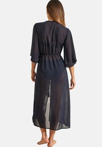 Robe transparente bleu marine avec des manches trois-quarts, taille élastique et devant ouvert ; texture lisse avec un design fluide.