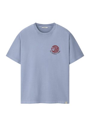 Mann mit lockigem Haar, der ein hellblaues, übergroßes T-Shirt mit kurzen Ärmeln trägt, von hinten vor einem beigen Hintergrund gezeigt.