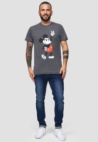 Šedé bavlněné tričko s potiskem Mickey Mouse v červeném oblečení. V kombinaci s tmavě modrými džíny a bílými teniskami.