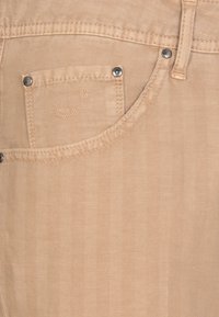 Jeans in denim beige con una texture a zigzag. Presentano una piccola tasca con accessori in argento e un logo ricamato sulla tasca.