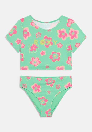 Dwuczęściowy kostium kąpielowy z krótkim topem z krótkim rękawem i majtkami w kolorze miętowym, pokryty jaskrawym różowym i żółtym wzorem kwiatowym oraz logo „ROXY” na topie.