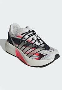 Sport shoe featuring a mesh upper in white and black, reflective accents, red detailing, and a cushioned sole with a textured finish.
