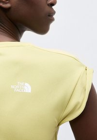 Κοντινό πλάνο ενός ατόμου που φοράει αμάνικη μπλούζα ανοιχτού κίτρινου χρώματος με το λογότυπο της The North Face στο πάνω μέρος της πλάτης.
