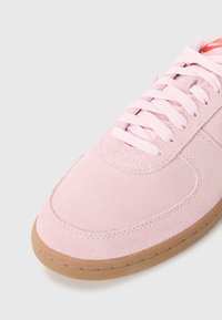 Rosa semskesneaker med rund tå, flate snørebånd og gummisåle. Har sydd detaljer langs midtsålen og vampen.