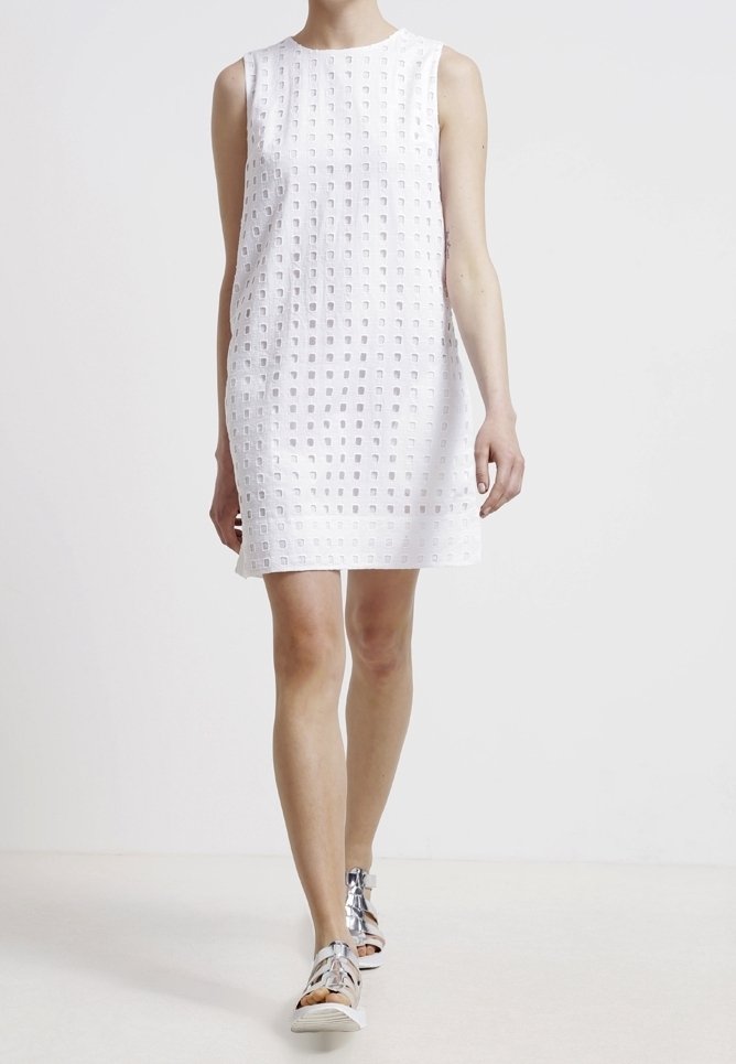 Robe blanche sans manches avec un motif en grille texturé, tissu léger et coupe droite. Associée à des baskets métalliques.