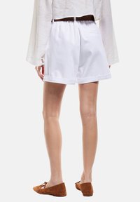 Shorts en coton blancs avec une coupe décontractée, dotés d'une taille élastique et de bords ourlés. La vue arrière montre un design de poche basique.