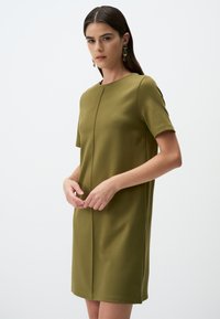 Olivengrünes Kurzarmkleid mit runder Ausschnittform, gerader Silhouette und Frontnahtdetails. Glatte Stoffstruktur.