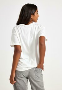 Vit bomulls-T-shirt med korta ärmar, rundad hals och en avslappnad passform, ihop med ljusgrå denimjeans med sidofickor.