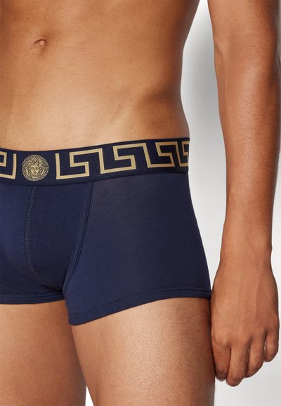 Marinefarbene Boxershorts aus weichem Stoff, mit einem goldakzentuierten Bund, der ein griechisches Schlüsselmotiv und ein Medusa-Logo zeigt.