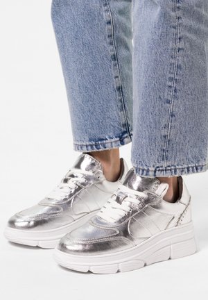 Silver metallic sneakers with white soles, featuring a smooth texture, lace-up design, and subtle stitching details. Worn with cropped jeans.