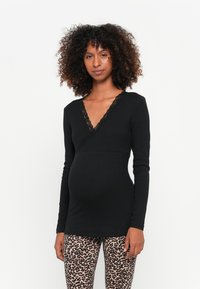 Maglietta nera a maniche lunghe con bordo in pizzo sul collo a V profondo e silhouette aderente, abbinata a leggings con stampa leopardata. Texture morbida, materiale elastico.