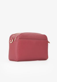 Borsa cosmetica rettangolare rossa realizzata in materiale sintetico testurizzato. Presenta due zip dorate e un anello laterale per il fissaggio o il trasporto.