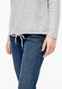 Maglione a maglia grigio chiaro con orlo coulisse e dettagli argento, abbinato a jeans in denim blu scuro con vestibilità slim.