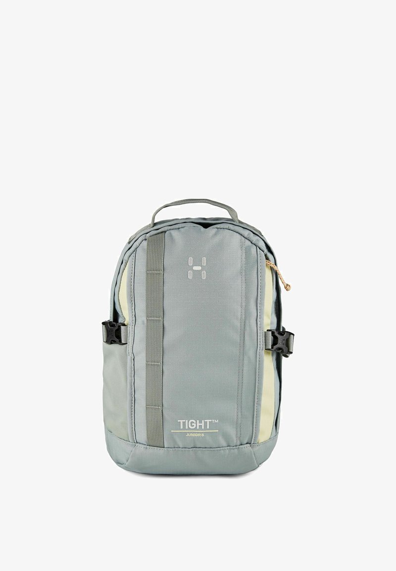 Petit sac à dos compact gris et beige avec une sangle verticale à l'avant, des boucles latérales, une poignée supérieure, et le texte « TIGHT Junior 8 » sur le panneau avant.