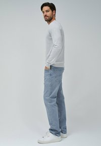 Hellgrauer Baumwollpullover mit langen Ärmeln, Rundhalsausschnitt, kombiniert mit hellblauen Jeans. Weicher Stoff und lockere Passform. Weiße Sneakers.