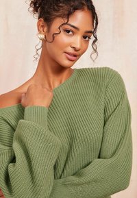Grüner Strickpullover mit geripptem Muster und übergroßen Ärmeln, im Off-the-Shoulder-Design und einem weichen, kuscheligen Look.