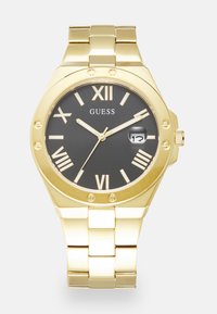 Montre dorée avec un cadran noir. Présente des chiffres romains, une fenêtre de date et un bracelet à maillons. Remarquable par son design de boîtier octogonal élégant.
