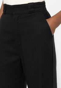Pantalones negros hechos de un tejido suave, con un frente plano, bolsillos laterales y un corte recto con una cinturilla ajustada.
