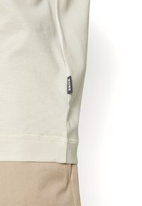 Světle béžové bavlněné tričko s černou cedulkou "BOSS" na bočním švu; hladká textura a jednoduchý design bez viditelných vzorů.