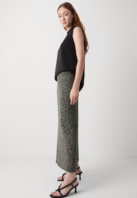 Top sin mangas negro combinado con una falda larga hasta los tobillos con un estampado en tonos de negro y crema. Usado con sandalias de tacón negras.