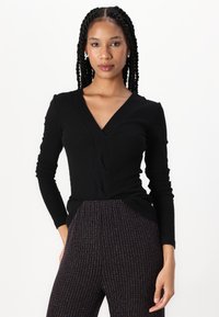 Black long-sleeve top with a v-neck and twisted front design, paired with textured black and multicolor ribbed pants.